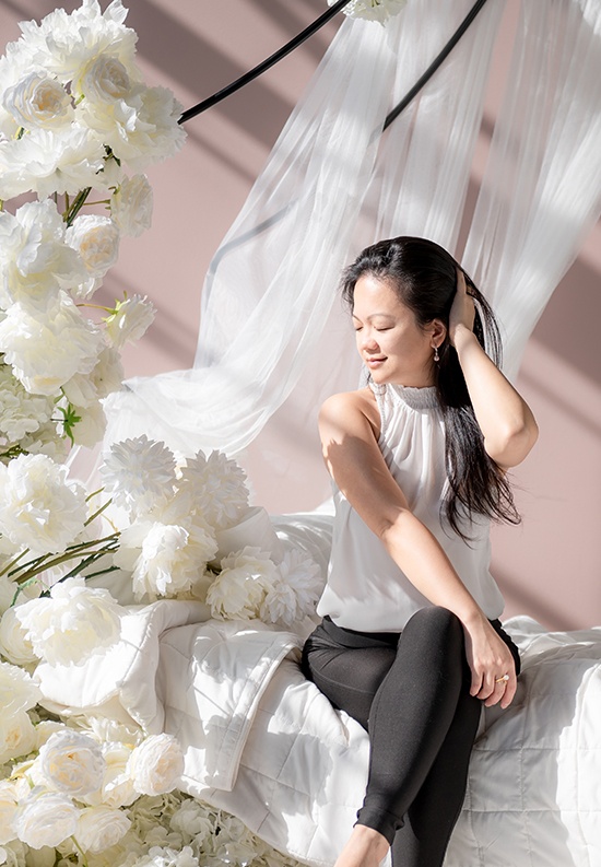 Professional Portrait Photography of a girl sitting on a bed with white flowers by Flores Photography