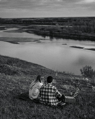 Photograph in black and white of a couple relaxing by a lovely river landscape captured by Darkstrand Visuals