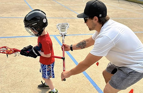 A Lacrosse Coach providing individualized coaching, assisting a young boy with a lacrosse stick.