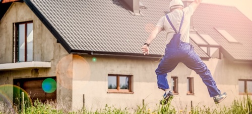 A handyman jumping happily in front of a house