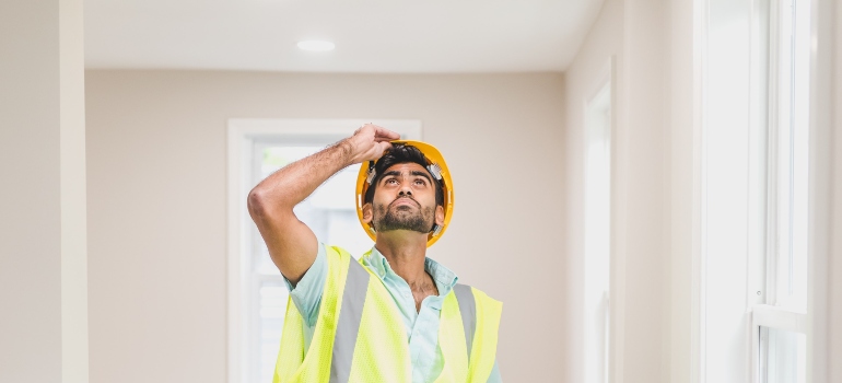 A home inspector looking up while holding his helmet.