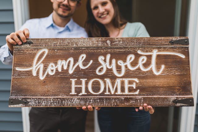Smiling couple holding a wooden HOME SWEET HOME sign