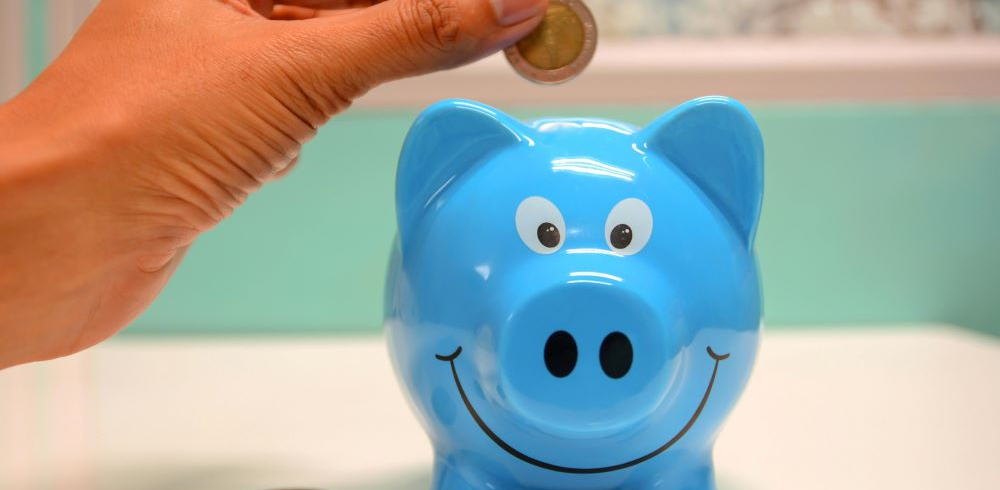 A hand putting a coin in a blue piggy bank