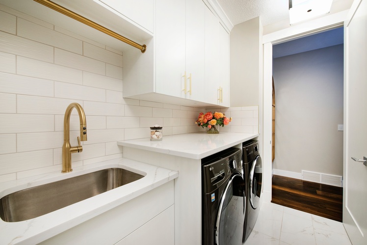 A WHITE AND GREY QUARTZ COUNTERTOP PAIRED WITH WHITE CABINETS AND TILES GIVE YOUR LAUNDRY ROOM A CLEANER, BRIGHTER AND FRESHER FEEL.