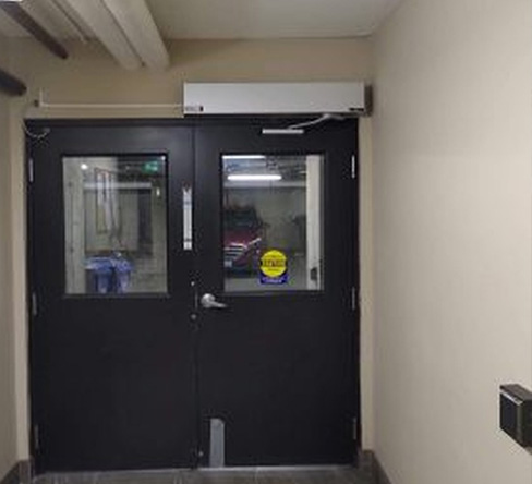 A black door with a yellow sign on it, having the automatic door closer installed by Integral Konnect.