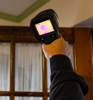 Professional conducting a home inspection with a thermal device to identify potential issues