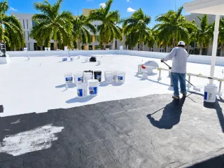 Worker applying a white coating to a flat roof