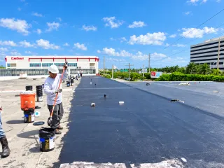 Crew rolling a dark coating onto a commercial flat roof