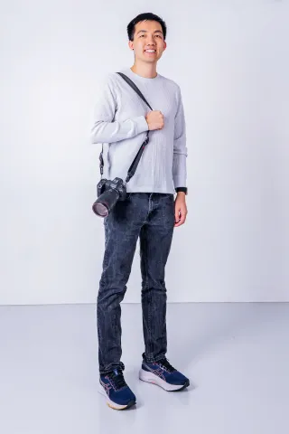 Brand portrait of a professional photographer holding a DSLR camera in a white studio.