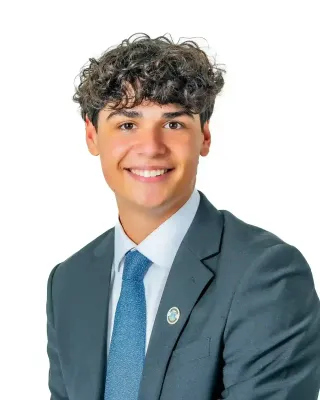 Professional headshot of a young man in a dark suit and blue tie against a white background.